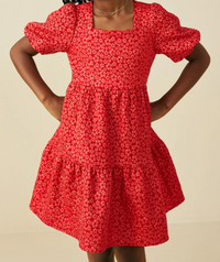 A red tiered dress with a small white floral pattern, featuring puff sleeves and a square neckline, shown on a model against a plain beige background.