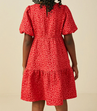 A red short-sleeve tiered dress with a small white floral pattern, shown from the back on a model against a light beige background.