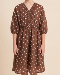 A brown V-neck midi dress with white polka dots, featuring puff sleeves, a smocked waist, and front button details, shown on a model against a beige background.