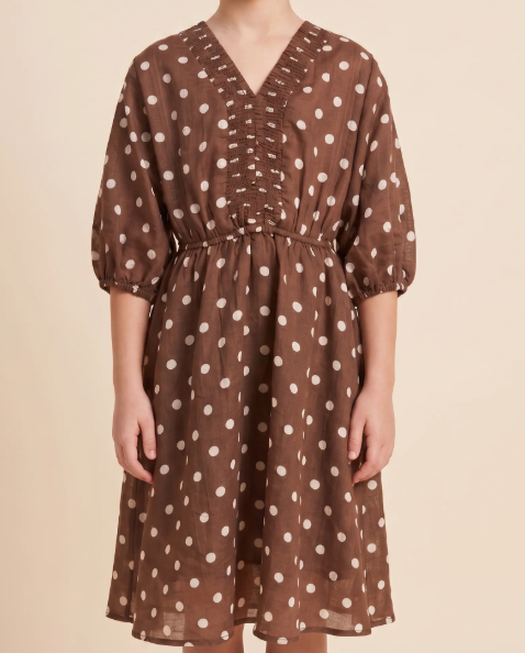 A brown V-neck midi dress with white polka dots, featuring puff sleeves, a smocked waist, and front button details, shown on a model against a beige background.
