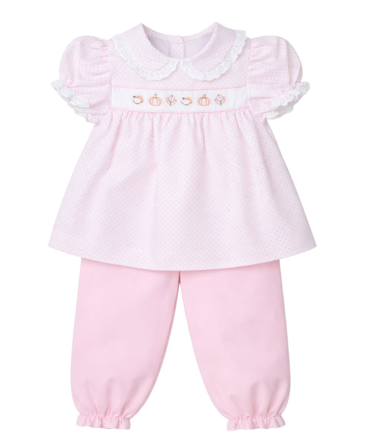 A baby girl's two-piece outfit consisting of a light pink short-sleeve top with a Peter Pan collar, white lace trim, and a smocked chest panel with embroidered pumpkins, paired with matching light pink pants with elastic cuffs.