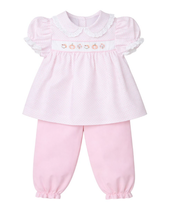 A baby girl's two-piece outfit consisting of a light pink short-sleeve top with a Peter Pan collar, white lace trim, and a smocked chest panel with embroidered pumpkins, paired with matching light pink pants with elastic cuffs.