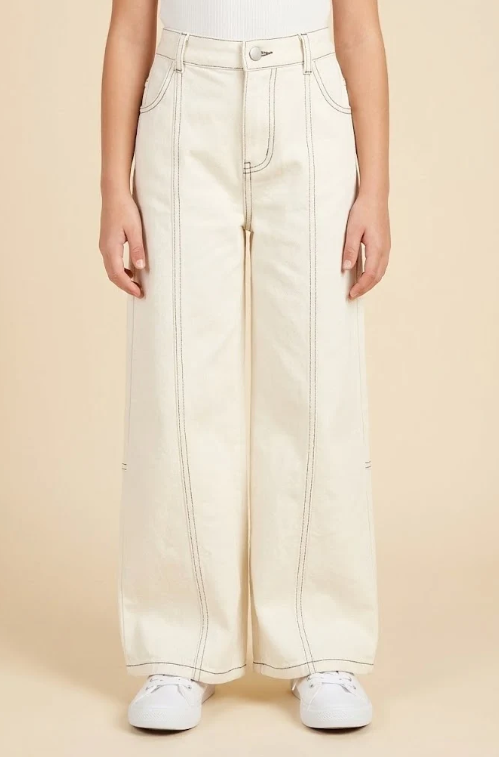A person wearing off-white wide-leg jeans with contrast stitching, paired with white sneakers, shown from the waist down against a solid beige background.