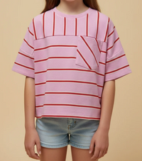 A child wearing a pink short-sleeve top with red horizontal stripes and a diagonal striped chest pocket, paired with light blue denim shorts, against a solid beige background.