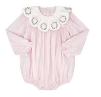 A baby long-sleeve bodysuit in light pink, featuring a large white ruffled collar decorated with embroidered green wreaths and pink bows, set against a solid gray background.