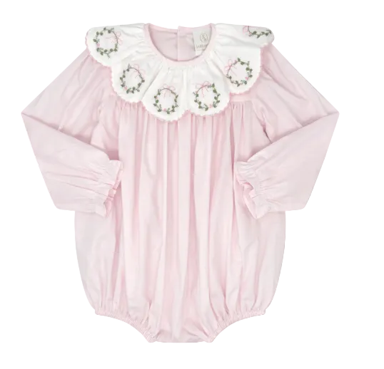 A baby long-sleeve bodysuit in light pink, featuring a large white ruffled collar decorated with embroidered green wreaths and pink bows, set against a solid gray background.