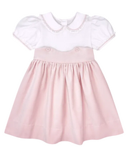 A baby girl's short-sleeve dress with a white batiste Peter Pan collar top and a pleated light pink skirt, shown against a solid gray background.