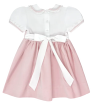 A baby girl's short-sleeve dress with a white batiste and lace bodice, featuring a pink skirt and a large white ribbon bow at the waist, shown against a solid gray background.
