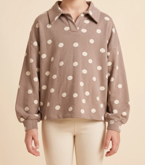 A person wearing a taupe-brown long-sleeve polo shirt with white polka dots, paired with cream pants, against a solid beige background.