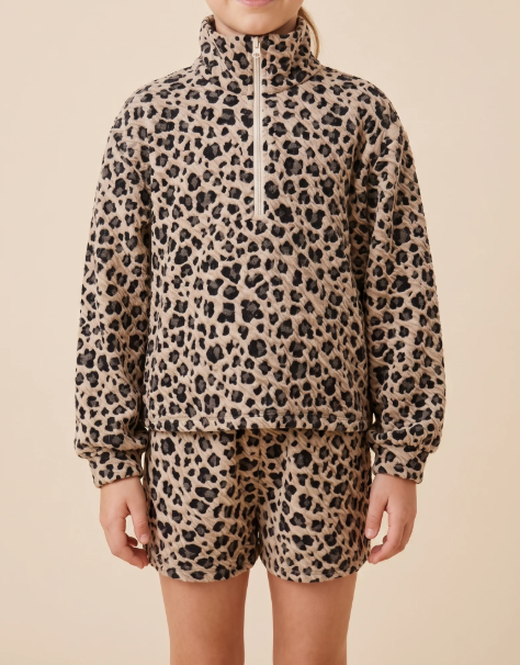 A child wearing a matching beige and black leopard-print fleece set, featuring a long-sleeve half-zip pullover and matching shorts, against a solid beige background.