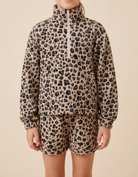 A child wearing a matching beige and black leopard-print fleece set, featuring a long-sleeve half-zip pullover and matching shorts, against a solid beige background.