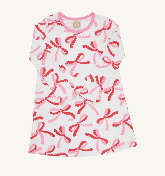 A white long-sleeve t-shirt dress featuring an all-over pattern of pink and red bow motifs, with a pink collar and a circular gold logo patch on the inside neck.