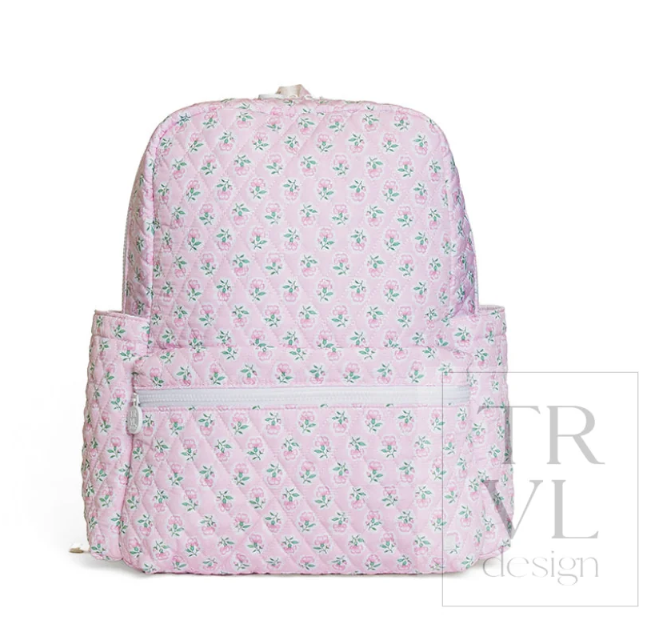 A pink quilted backpack with a repeating green and white floral pattern, featuring a front zippered pocket, photographed against a plain white background with a faint 'TRVL design' watermark.