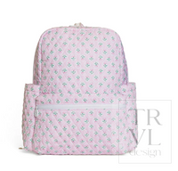 A pink quilted backpack with a repeating green and white floral pattern, featuring a front zippered pocket, photographed against a plain white background with a faint 'TRVL design' watermark.