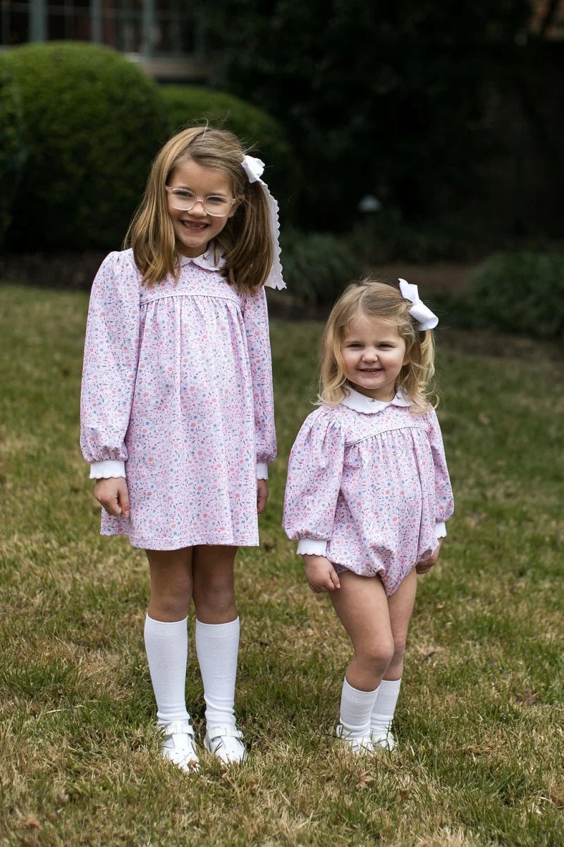 Two young girls in matching pink dresses standing on grass.