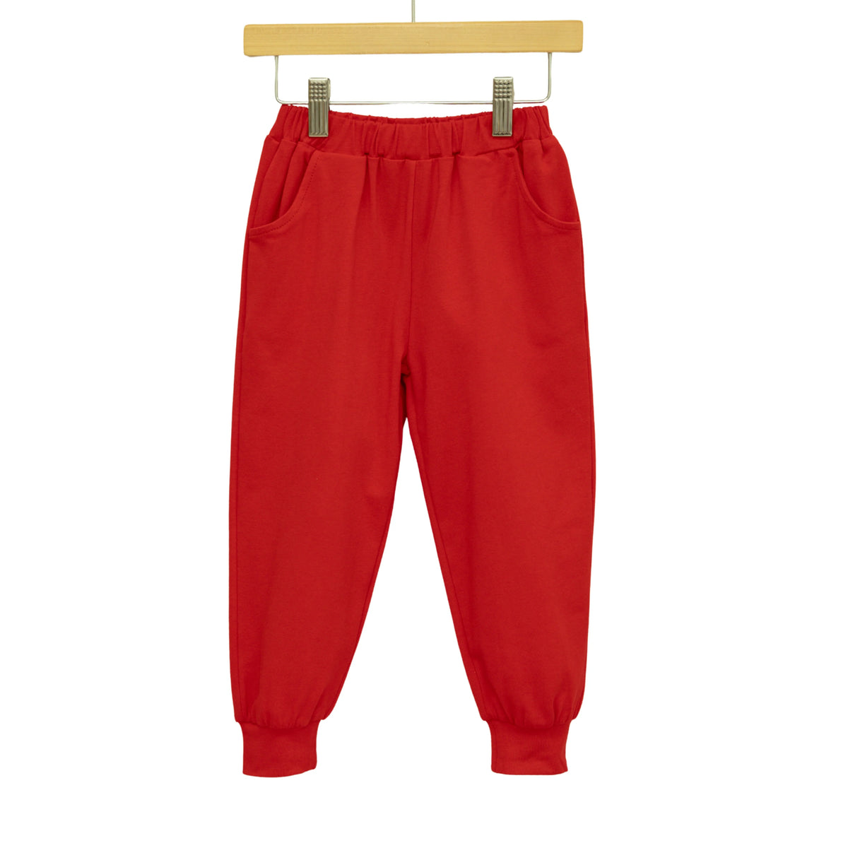 Red jogger pants with an elastic waistband and side pockets, hanging from a wooden hanger against a white background.