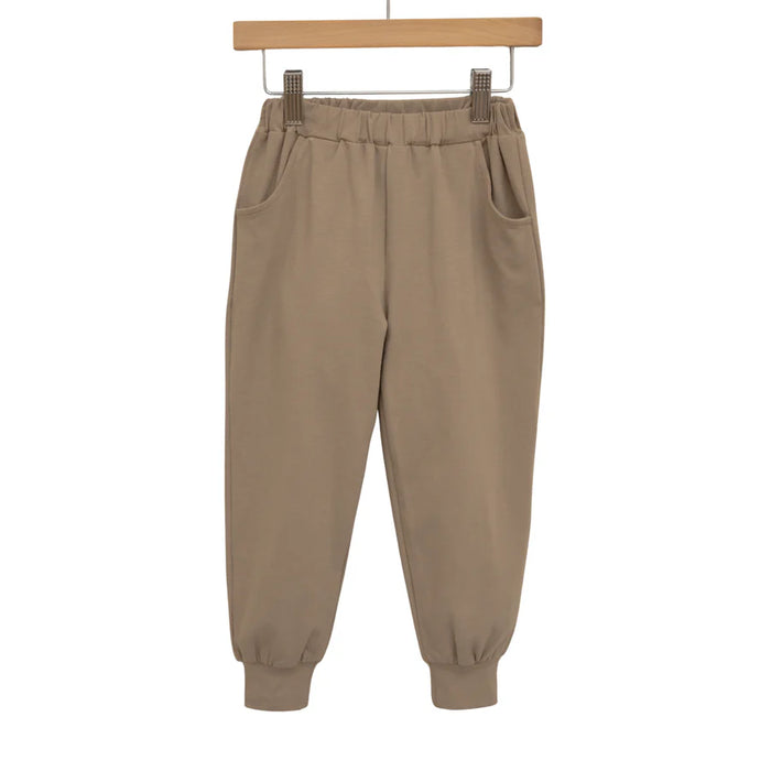 Beige sweatpants on a wooden hanger against a white background