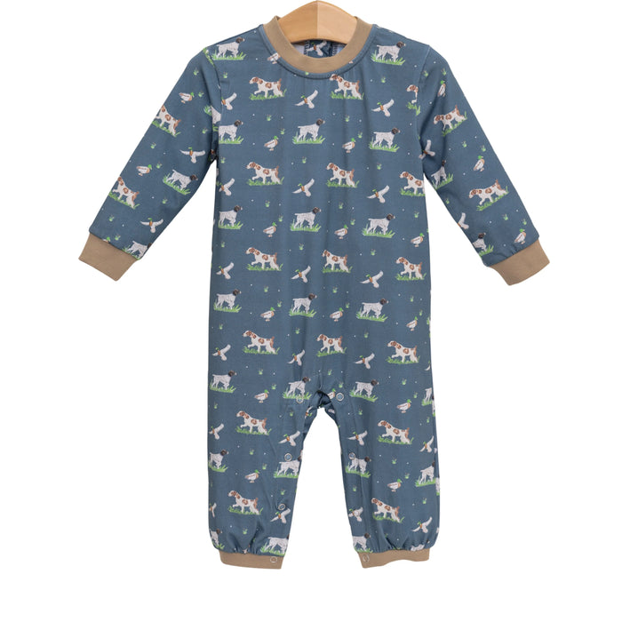 A baby long-sleeve footless jumpsuit in slate blue, featuring an all-over print of cows, sheep, and birds on a grassy background. The garment has tan ribbed cuffs and hem and is displayed on a wooden hanger against a plain white background.