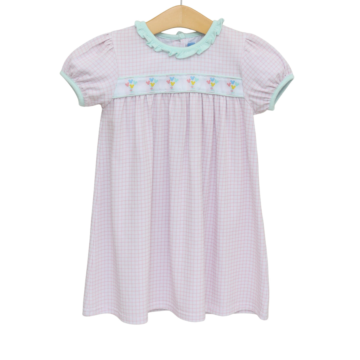 A short-sleeve baby girl's dress with a light pink and white gingham pattern, featuring a light green ruffled collar, a matching light green smocked chest band with embroidered flowers, and a wooden hanger.