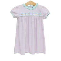 A short-sleeve baby girl's dress with a light pink and white gingham pattern, featuring a light green ruffled collar, a matching light green smocked chest band with embroidered flowers, and a wooden hanger.
