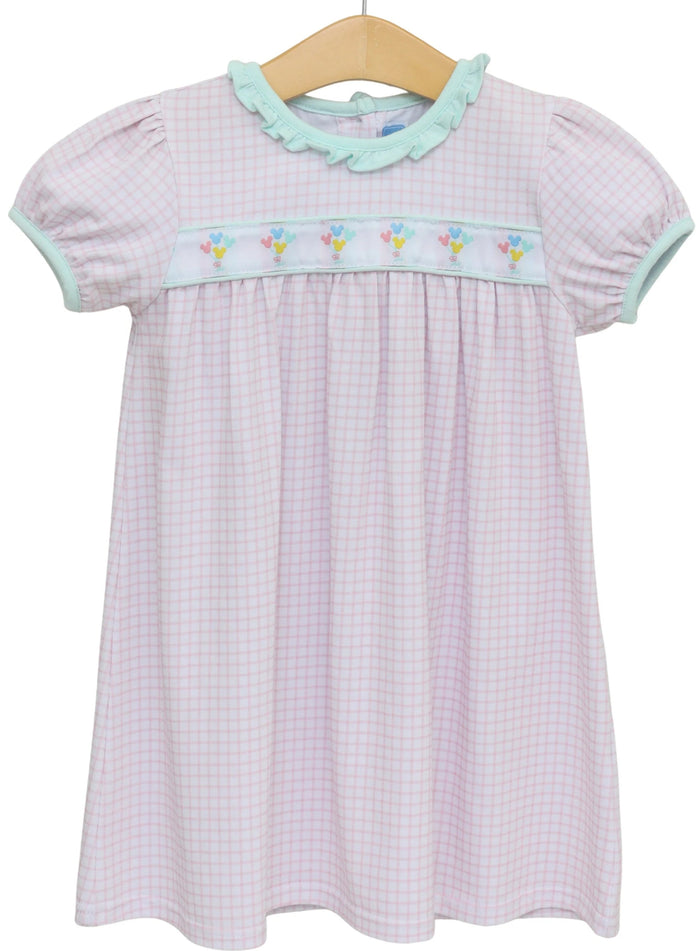 A short-sleeve baby girl's dress with a light pink and white gingham pattern, featuring a light green ruffled collar, a matching light green smocked chest band with embroidered flowers, and a wooden hanger.
