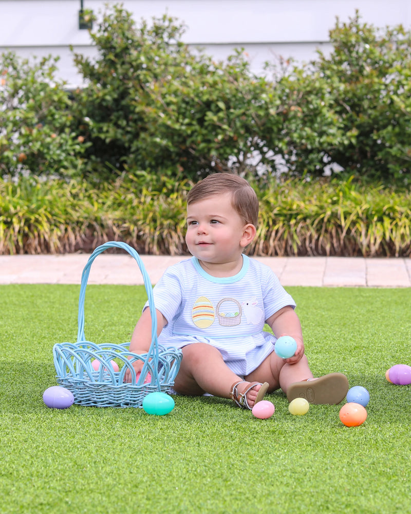 Child sitting on grass with Easter eggs and a basket