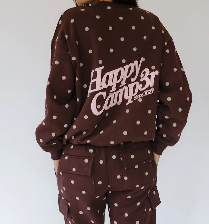 A woman shown from the back wearing a dark brown sweatshirt and matching cargo pants with white polka dots. The sweatshirt features a large white graphic text reading 'Happy Camp3r since 2009' across the back.