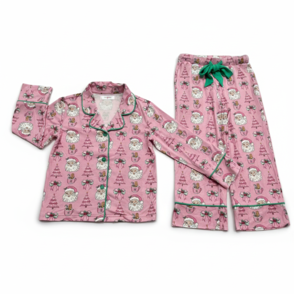 A two-piece pink pajama set featuring a long-sleeve button-front top and matching pants, both printed with a festive Santa Claus and Christmas tree pattern and finished with green piping and a green drawstring.