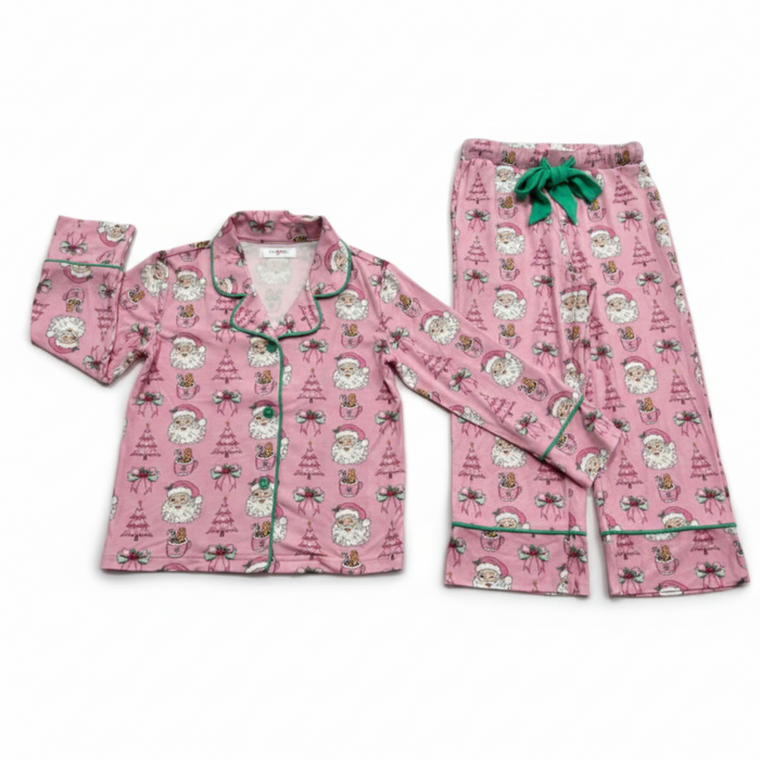 A two-piece pink pajama set featuring a long-sleeve button-front top and matching pants, both printed with a festive Santa Claus and Christmas tree pattern and finished with green piping and a green drawstring.