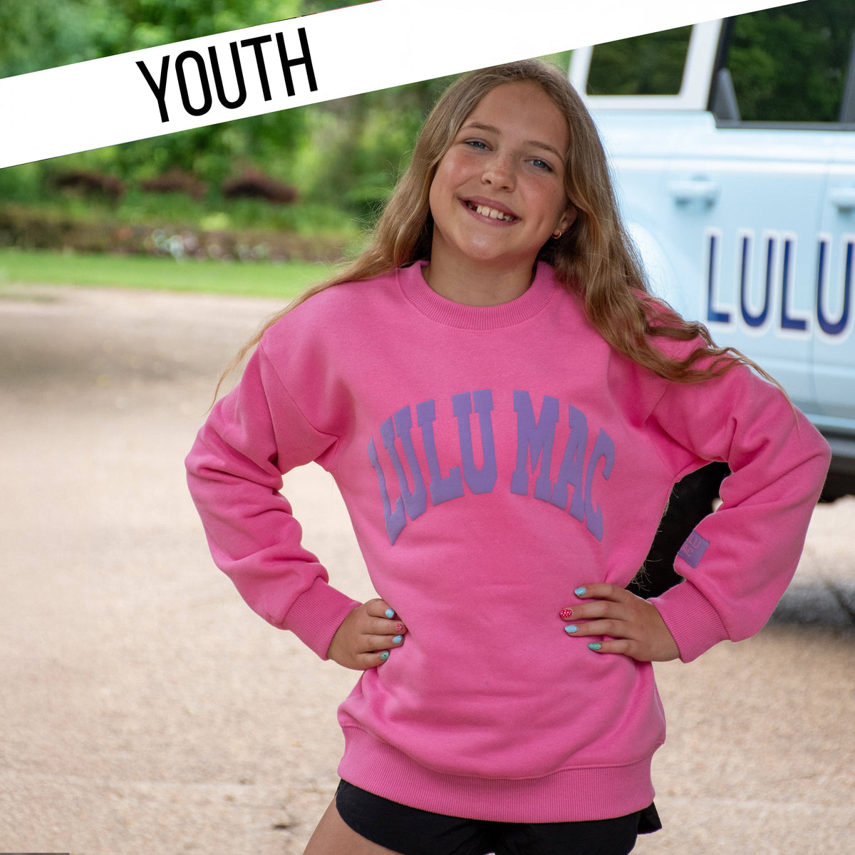 Person wearing a pink 'LULU MAC' sweatshirt with a blurred background