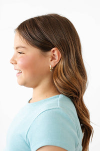 Side profile of a young girl with a ponytail wearing gold earrings on a white background