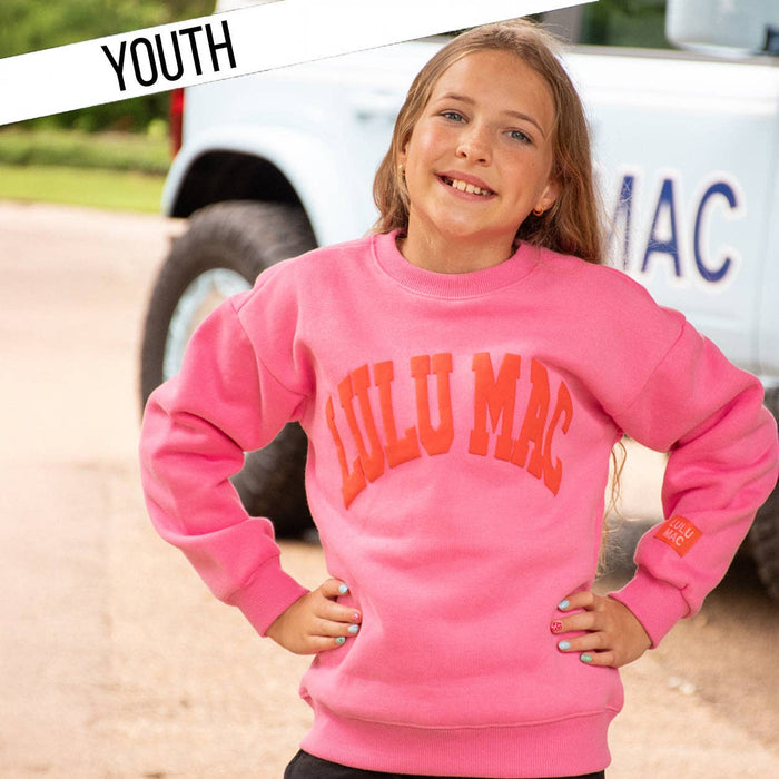 A young girl wearing a bright pink crewneck sweatshirt with 'LULU MAC' printed in orange across the chest, posing outdoors in front of a white pickup truck. A diagonal banner in the top left corner reads 'YOUTH'.