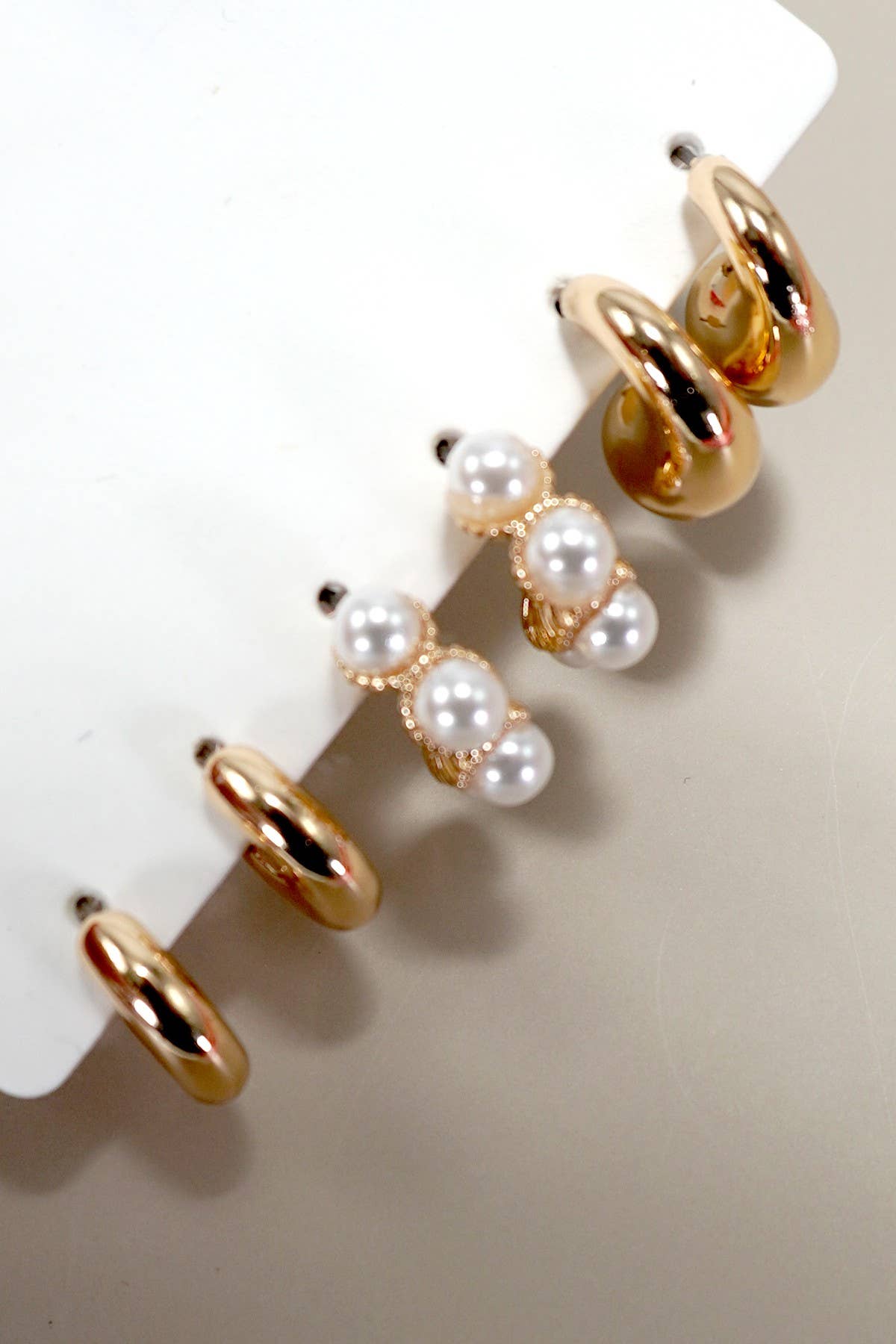 Gold hoop earrings with pearl accents on a white stand.