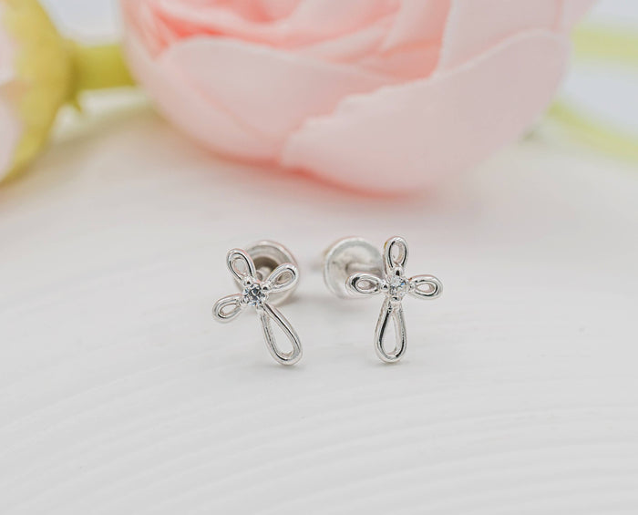 Silver cross-shaped earrings on a light background with a blurred floral background