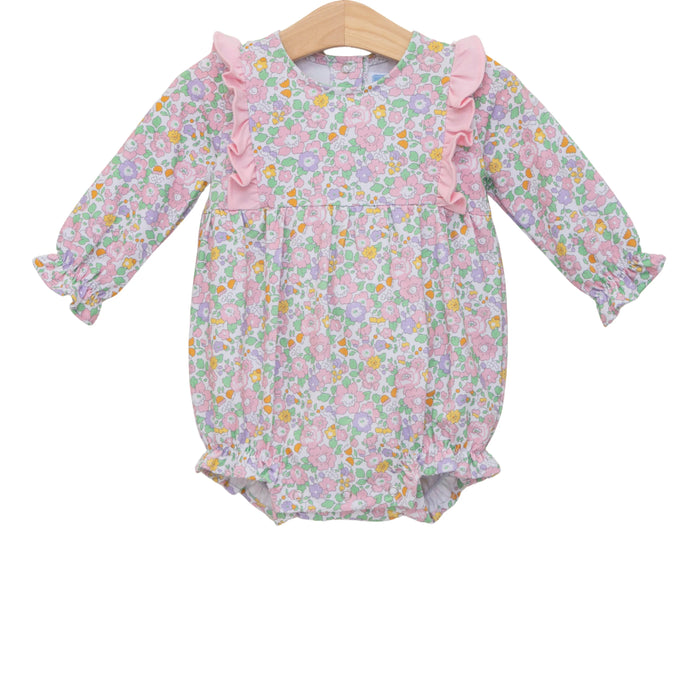 A baby girl's long-sleeve floral romper in pink, purple, and green, featuring ruffle details on the neckline and sleeves, displayed on a wooden hanger against a white background.
