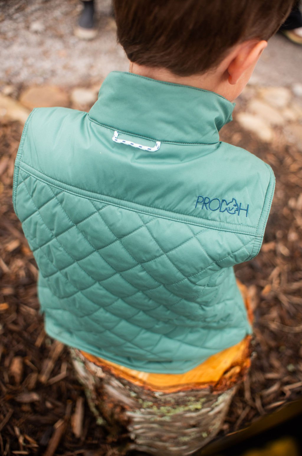 Child wearing a teal quilted vest with 'ProDen' branding outdoors.