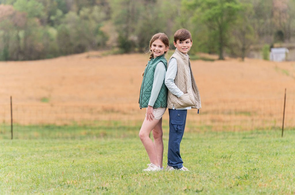 Two children standing back-to-back in a field with trees in the background