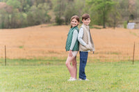 Two children standing back-to-back in a field with trees in the background