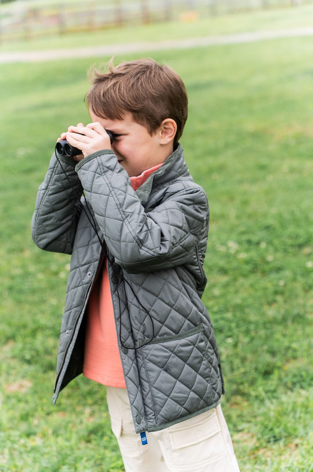 Child in a gray quilted jacket standing outdoors on grass