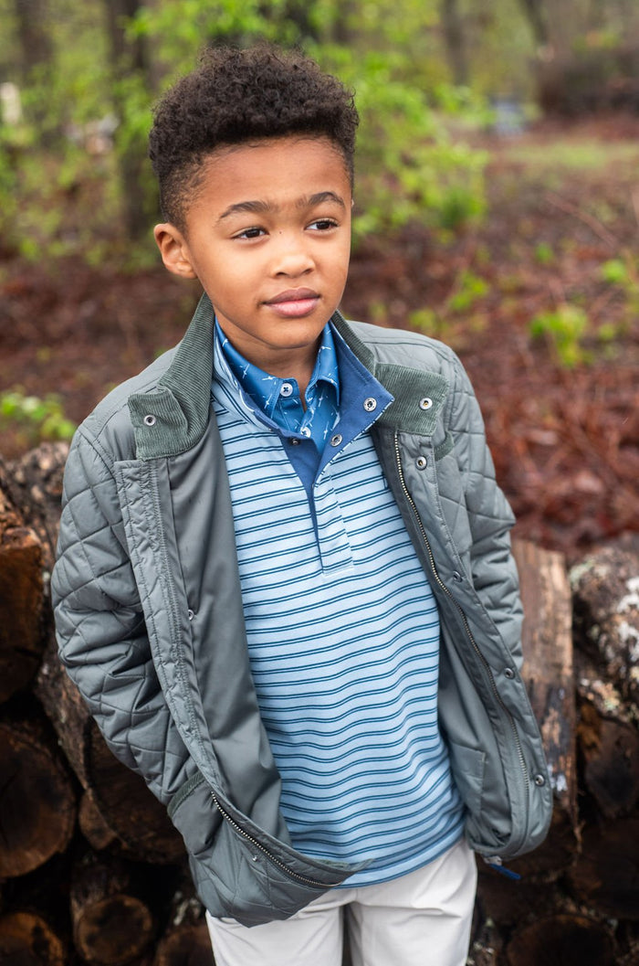 Young boy wearing a gray jacket over a blue striped shirt in a forest setting