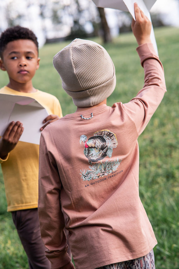 Person wearing a brown sweatshirt with a graphic design outdoors