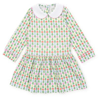 A long-sleeve baby dress with a white Peter Pan collar, featuring a green, pink, and red holiday pattern of Christmas trees and bows on a white background.