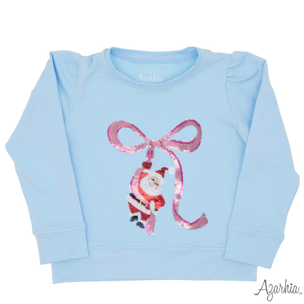 A light blue long-sleeve baby sweatshirt featuring a sequined pink bow and Santa Claus graphic on the front, with the brand name 'Agarkia' visible on the inner neck label and as a watermark in the corner.